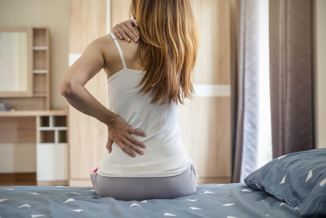 Femme assise sur un lit et se tenant le dos